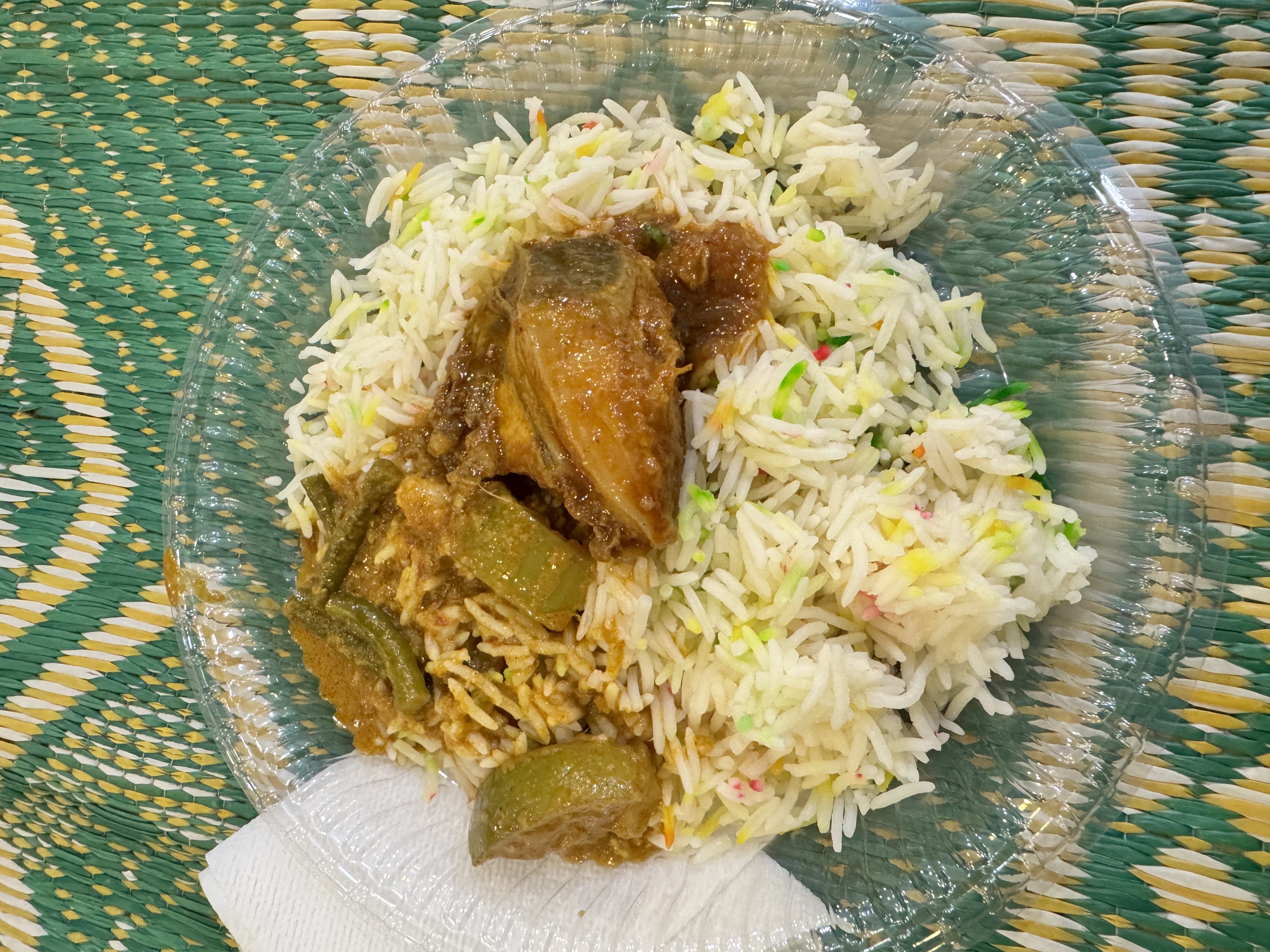 A plate of rice with chicken curry on a clear plastic plate.