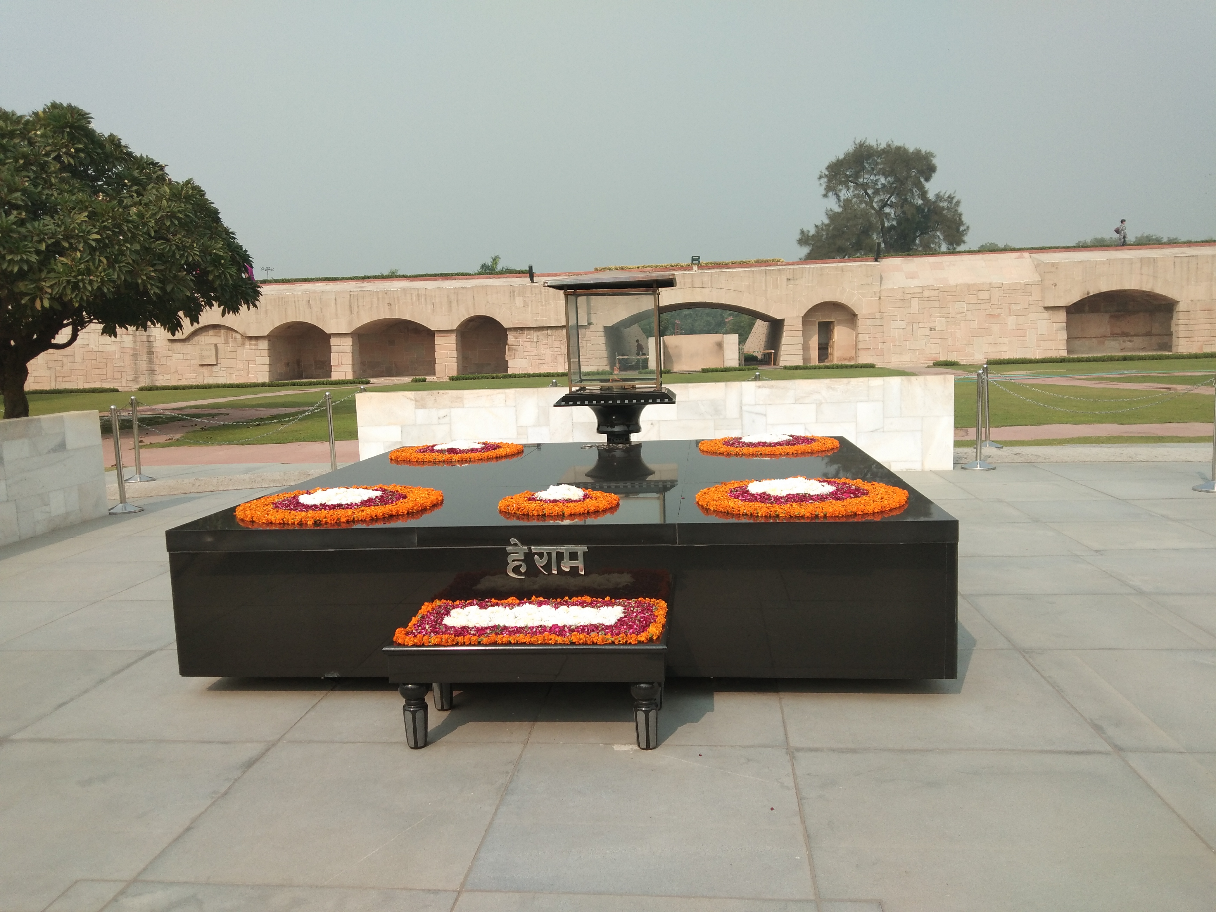 Mahatma Gandhi's memorial at Raj Ghat in Delhi, featuring a black marble platform adorned with circular flower arrangements and the inscription "हे राम" (Hey Ram), surrounded by a well-maintained garden and stone pathways.