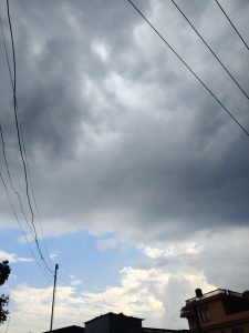 A cloudy sky is depicted with dark gray clouds dominating the upper part of the image, while patches of blue sky are visible peeking through.