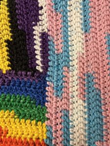 Close-up of three connected sections of crochet stitches in rainbow, trans, and nonbinary colors.