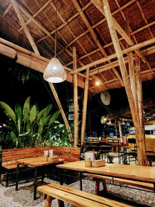 Cozy open-air café in Siargao, Philippines, featuring bamboo architecture, wooden seating, and warm ambient lighting. Surrounded by tropical plants, the space creates a relaxed island vibe perfect for a laid-back evening.