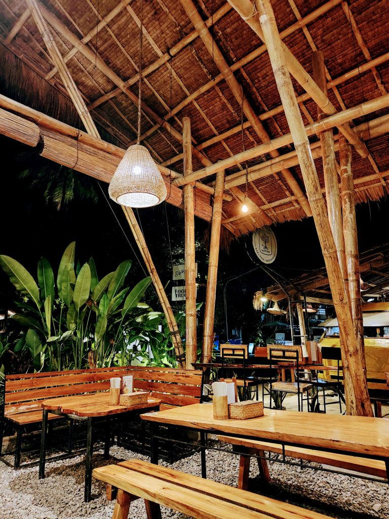 Cozy open-air café in Siargao, Philippines, featuring bamboo architecture, wooden seating, and warm ambient lighting. Surrounded by tropical plants, the space creates a relaxed island vibe perfect for a laid-back evening.