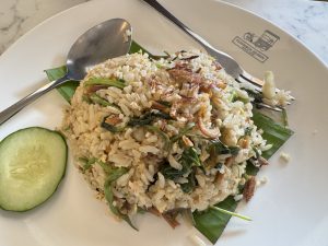 A plate of fried rice with vegetables and a slice of cucumber.