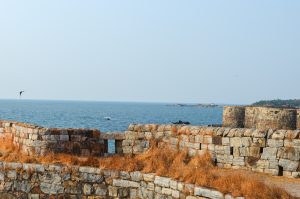 A scenic view of a rocky coastal landscape featuring weathered stone walls in the foreground.