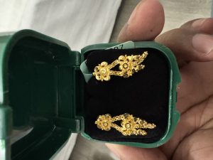A pair of gold earrings with floral designs in a green box.
