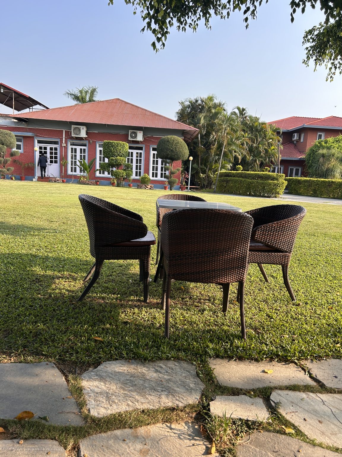 A peaceful outdoor setting featuring three wicker chairs arranged around a small table on a lush green lawn.