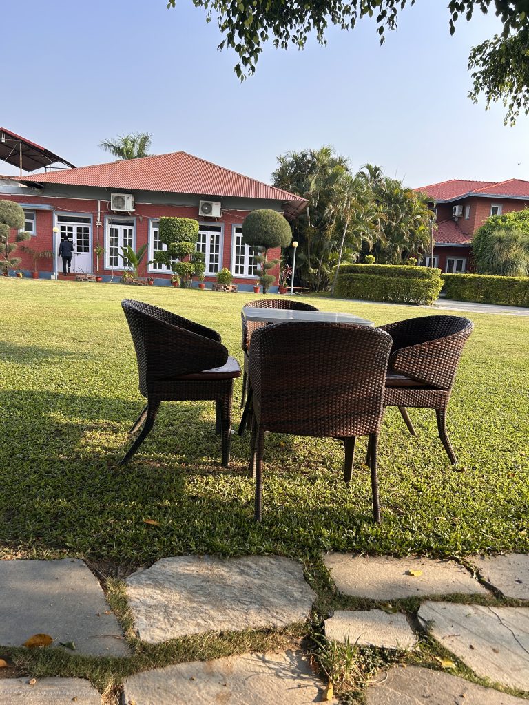 A peaceful outdoor setting featuring three wicker chairs arranged around a small table on a lush green lawn.