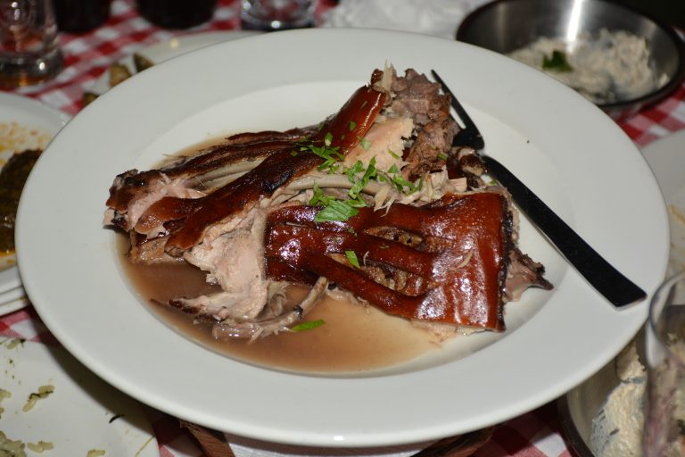 Roasted lechon with crispy skin and tender meat sits in savory broth, garnished with herbs. Captured in Paphos, Cyprus.