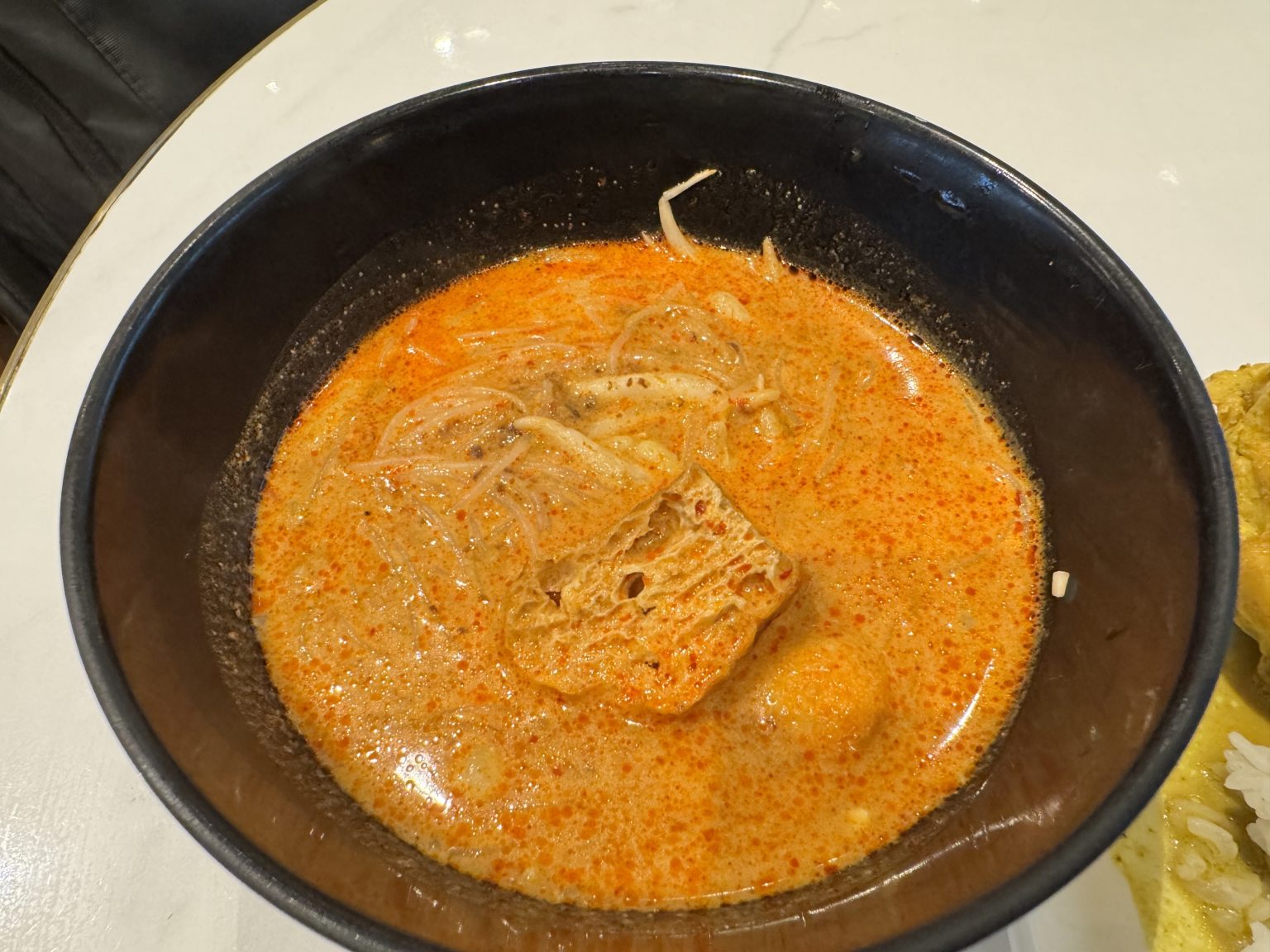 A bowl of spicy noodle soup with tofu and bean sprouts in orange broth.