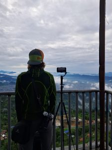 A person stands at the edge of a viewpoint overlooking a mountainous landscape.