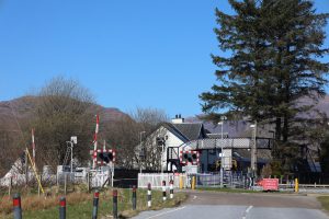 A scenic view of a railway crossing with a small building in the background. 

