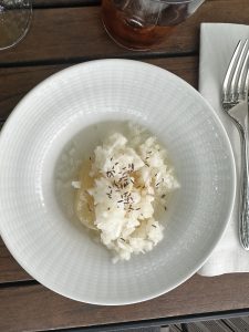 A light and refreshing dish featuring sliced potato topped with finely chopped raw onion and sprinkled with caraway seeds, served in a shallow bowl.