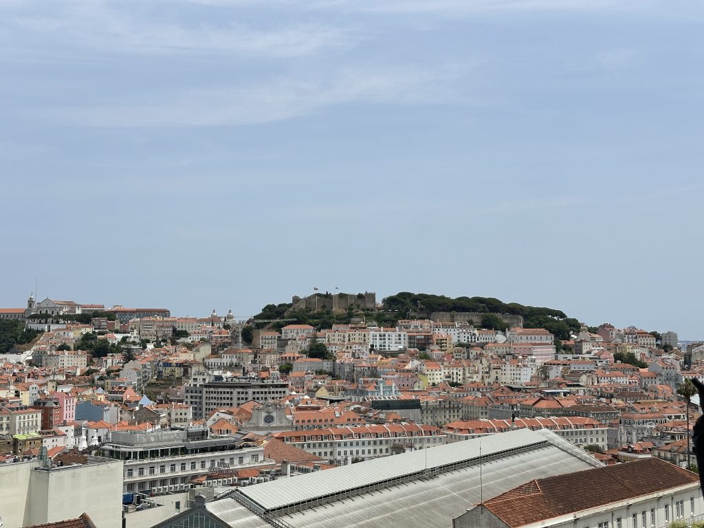 Overlooking Lisbon’s historic centre, this sweeping view captures the iconic São Jorge Castle perched atop the hill, surrounded by a patchwork of terracotta rooftops and pastel-coloured buildings that define the city’s timeless charm.