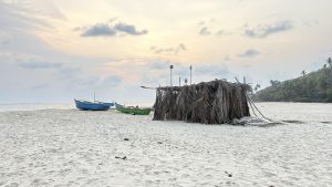 A sandy beach scene featuring a small thatched structure made of palm leaves.