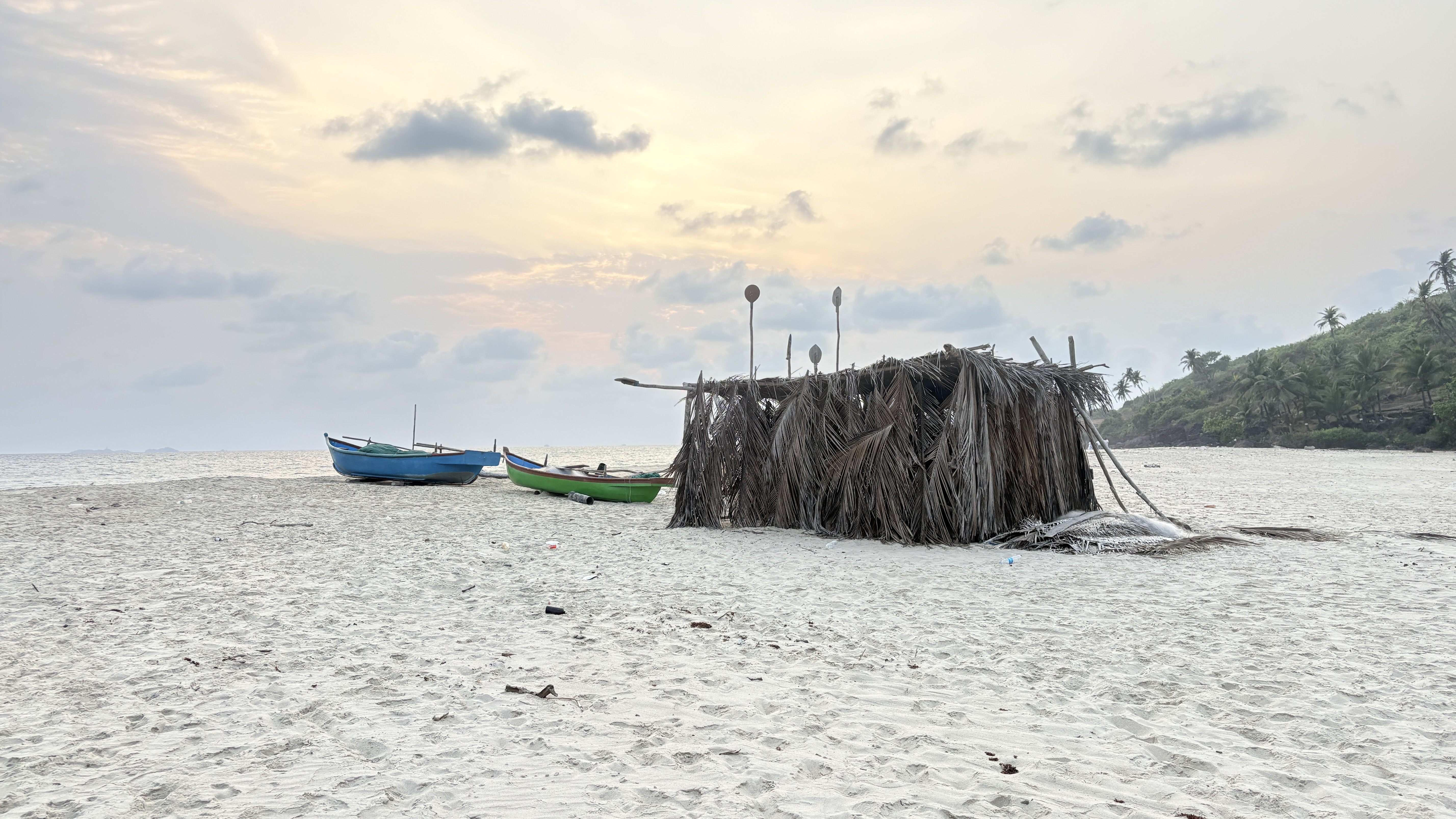A sandy beach scene featuring a small thatched structure made of palm leaves.