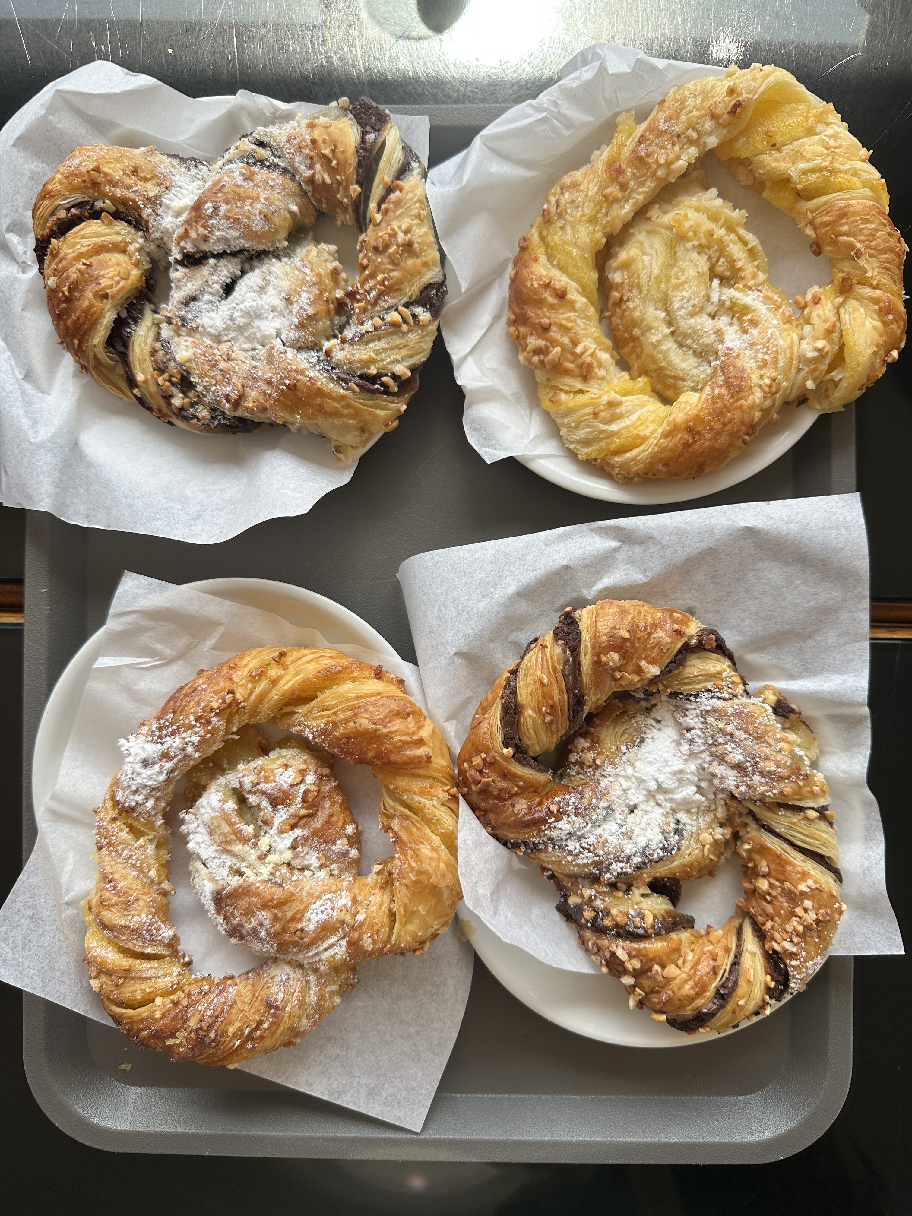 A delicious selection of Portuguese pastries, each golden and flaky with twisted layers, some filled with chocolate and others dusted with sugar or sprinkled with nuts—perfect companions to a morning coffee in Lisbon.