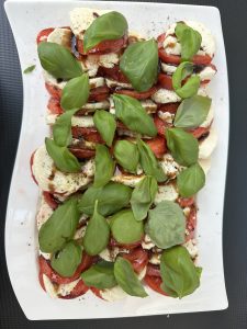 A vibrant Caprese salad made with alternating slices of fresh mozzarella and ripe tomatoes, topped with basil leaves and a drizzle of balsamic glaze, served on a white platter.