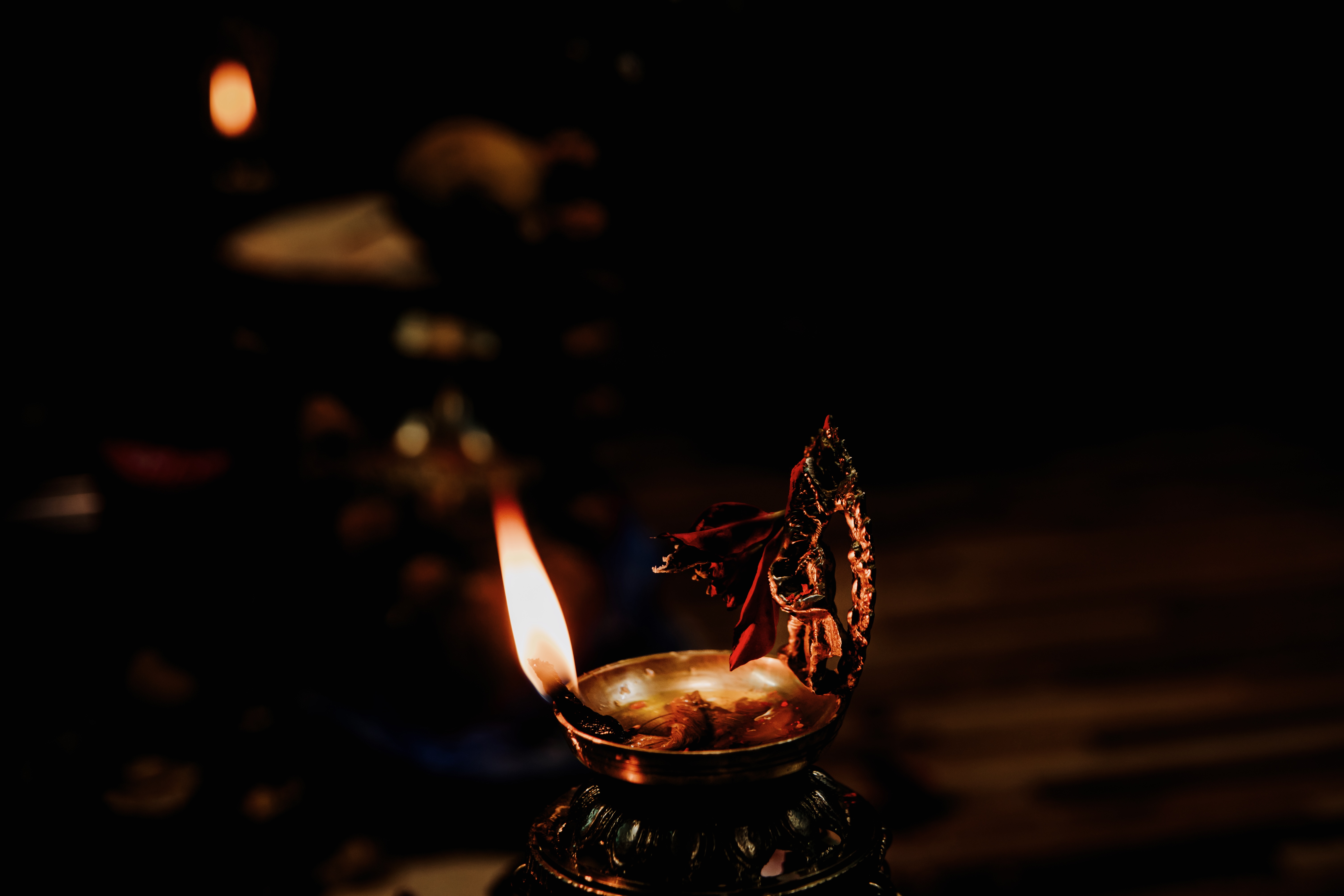 A glowing oil lamp with a flickering flame sits on a dark surface.
