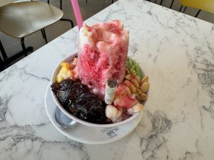 A bowl of shaved ice dessert with syrup, nuts, and various toppings.