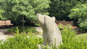 A stylized concrete bear sitting in some bushes.