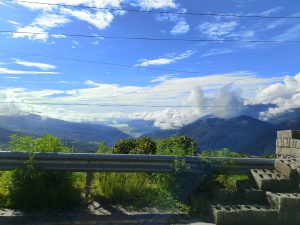 A scenic view of a mountainous landscape under a bright blue sky with scattered clouds.