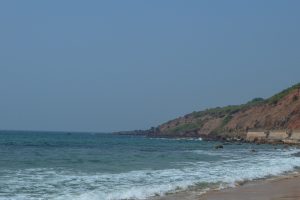 A serene beach scene featuring gentle waves lapping at the shore, with a rocky coastline and lush greenery along the hills in the background.