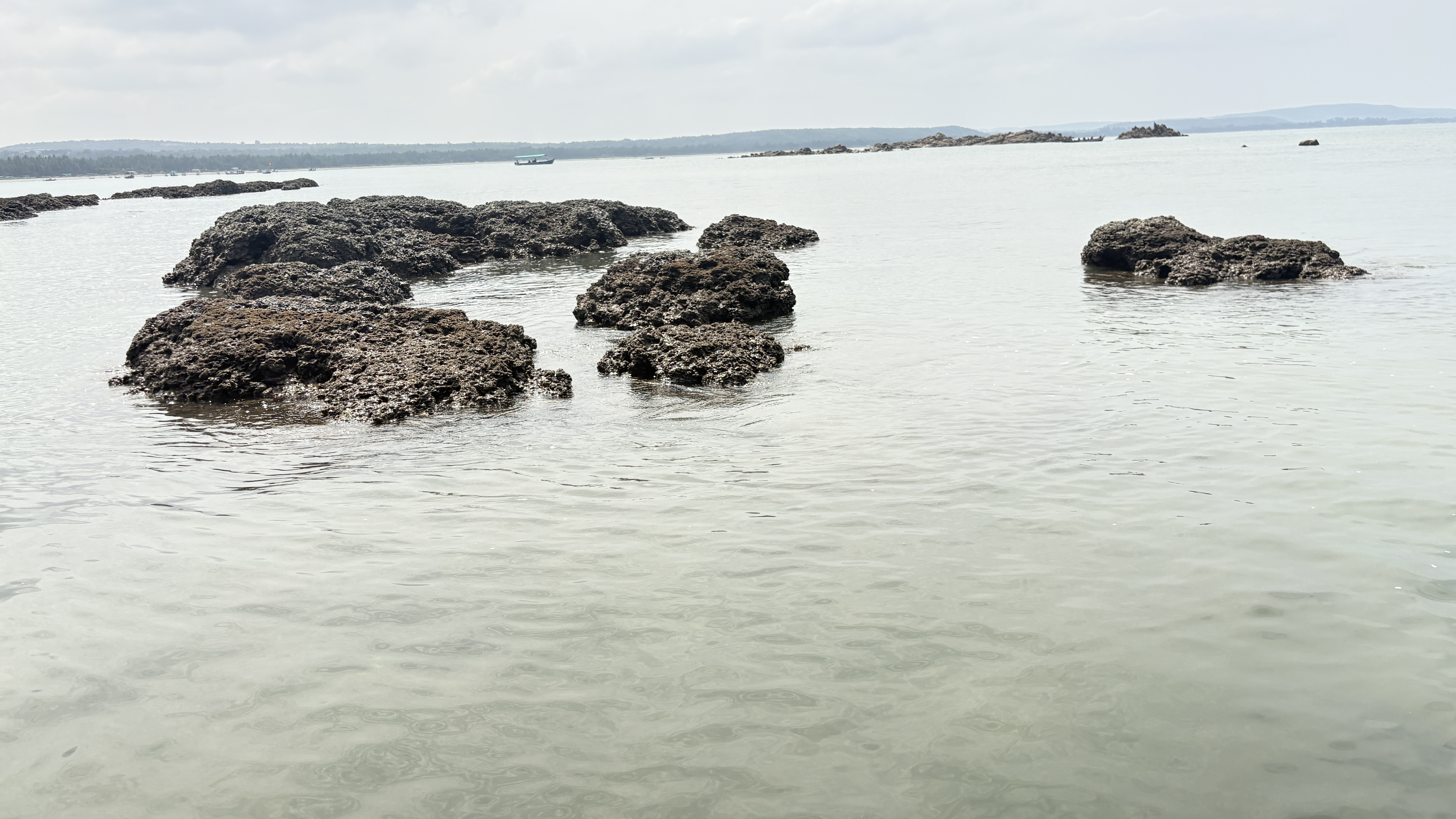 The image shows a serene coastal landscape with several rocky formations partially submerged in calm, clear water.