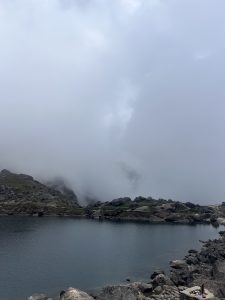 A serene landscape featuring a tranquil lake nestled among rocky terrain and majestic mountains, all enveloped in a soft veil of mist and drifting clouds.