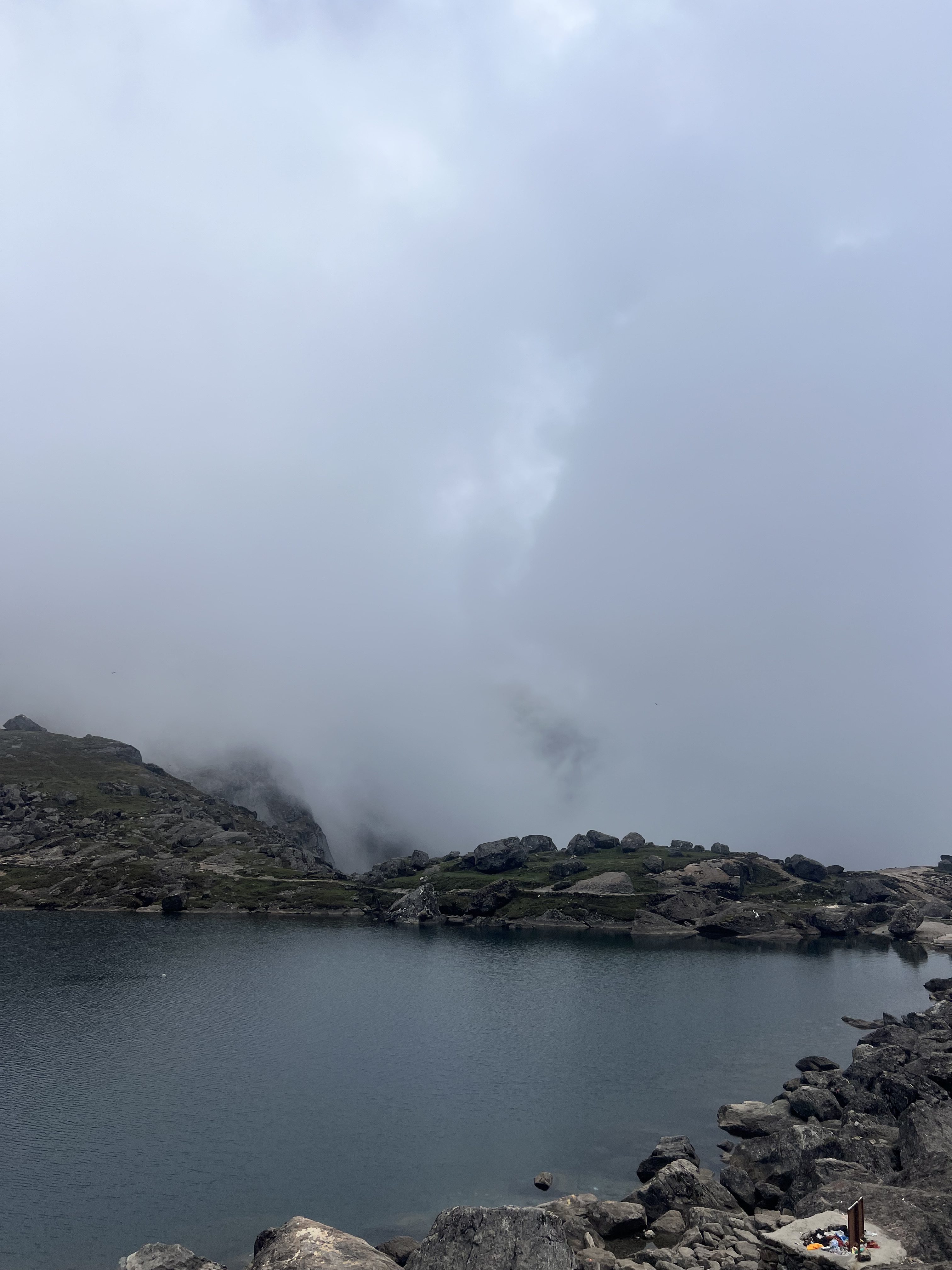 A serene landscape featuring a tranquil lake nestled among rocky terrain and majestic mountains, all enveloped in a soft veil of mist and drifting clouds.