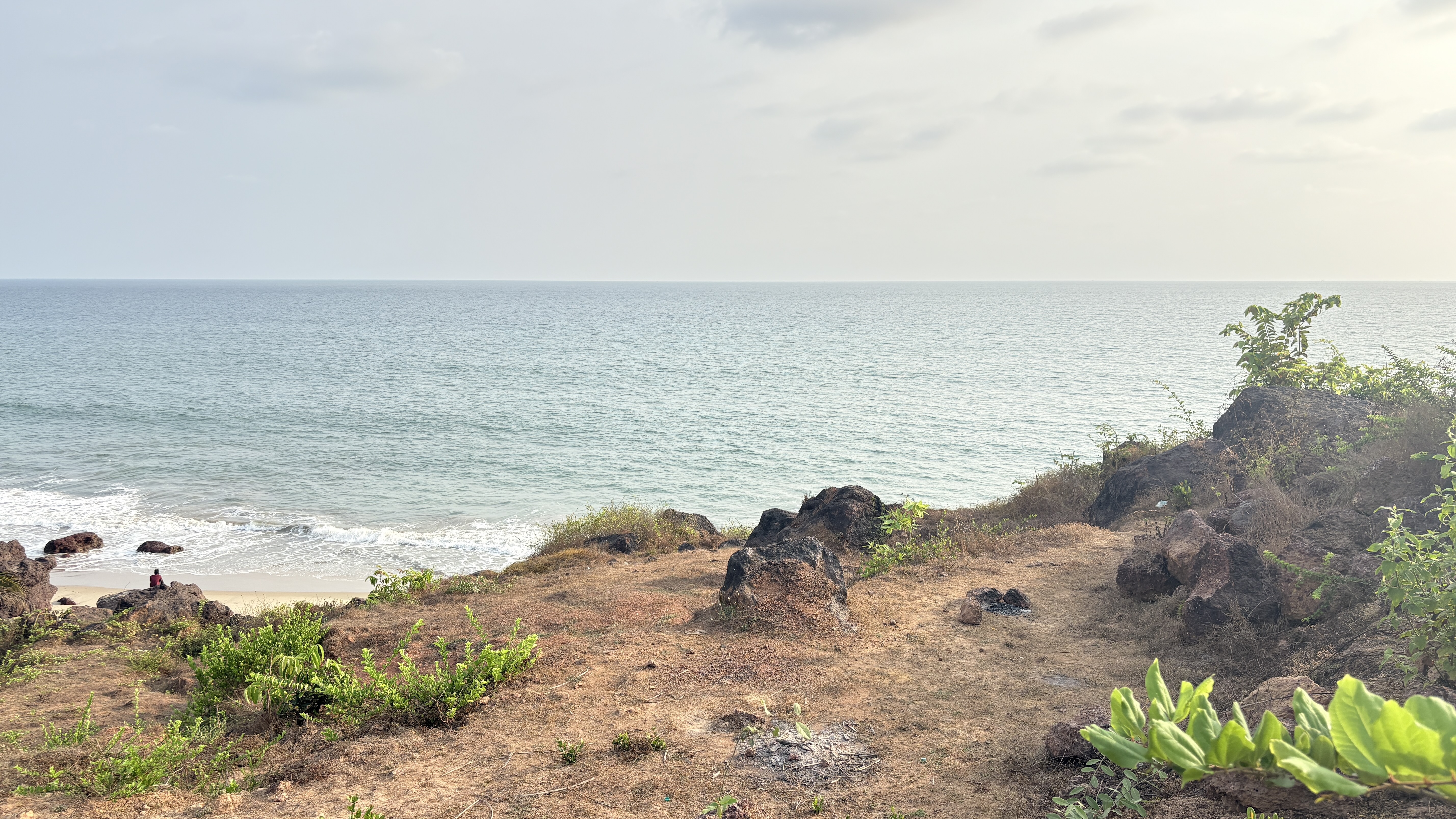 A serene seaside view featuring gentle waves lapping at a sandy beach, framed by grassy hills and scattered rocks.