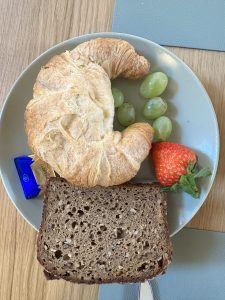 A whilte plate full of brown bread, butter and fruits. 