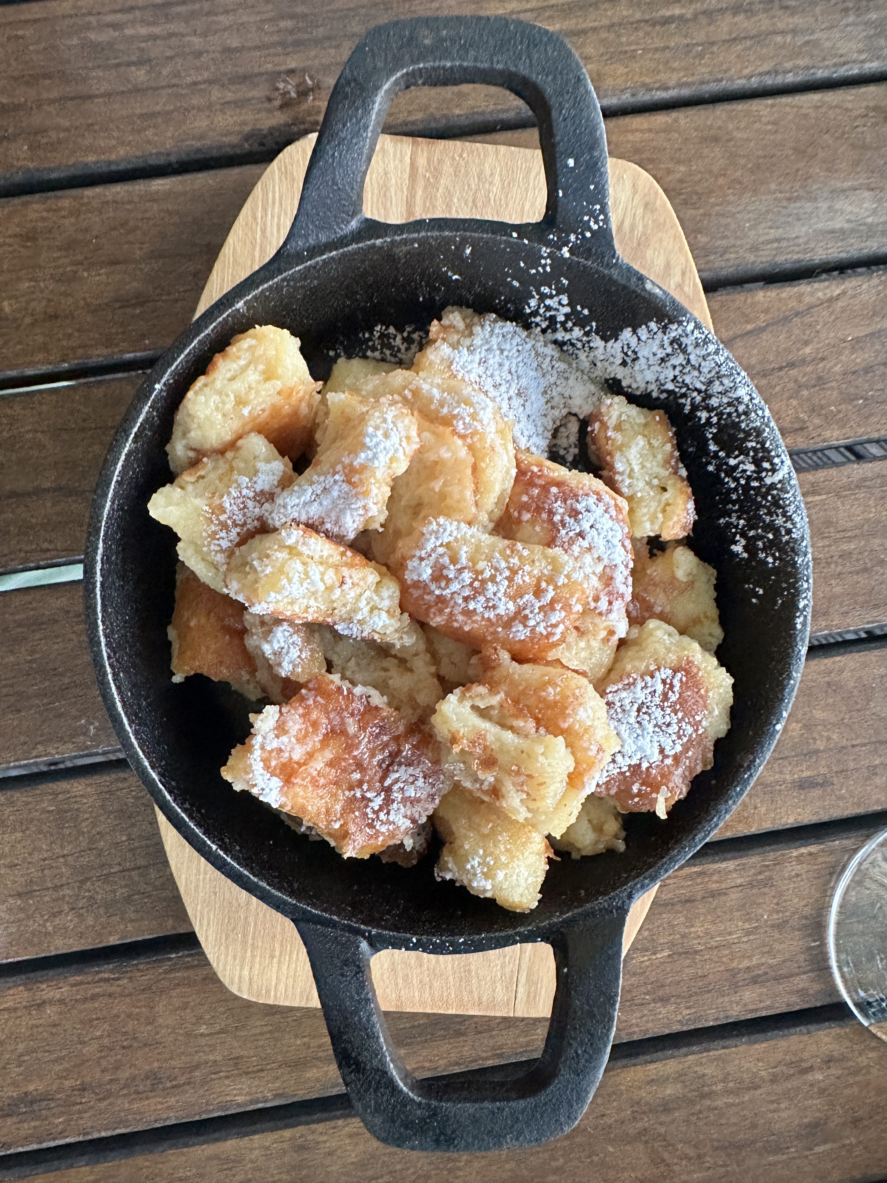 Golden pieces of shredded pancake, lightly dusted with powdered sugar, are served in a rustic cast-iron skillet — a classic presentation of the Austrian dessert Kaiserschmarrn.