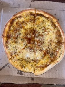 A freshly baked pizza with a golden-brown crust, topped with a layer of melted cheese and sprinkled with herbs, is placed inside a cardboard pizza box.