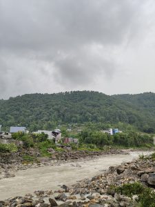 A river flows through a rocky landscape with a backdrop of lush green hills under a cloudy sk