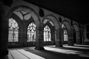 A black and white photograph showcasing a spacious interior with tall, arched windows featuring intricate detailing.
