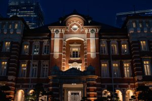 A front view of JR Tokyo Station at night. The interior lights are on, and the station is lit up from below.