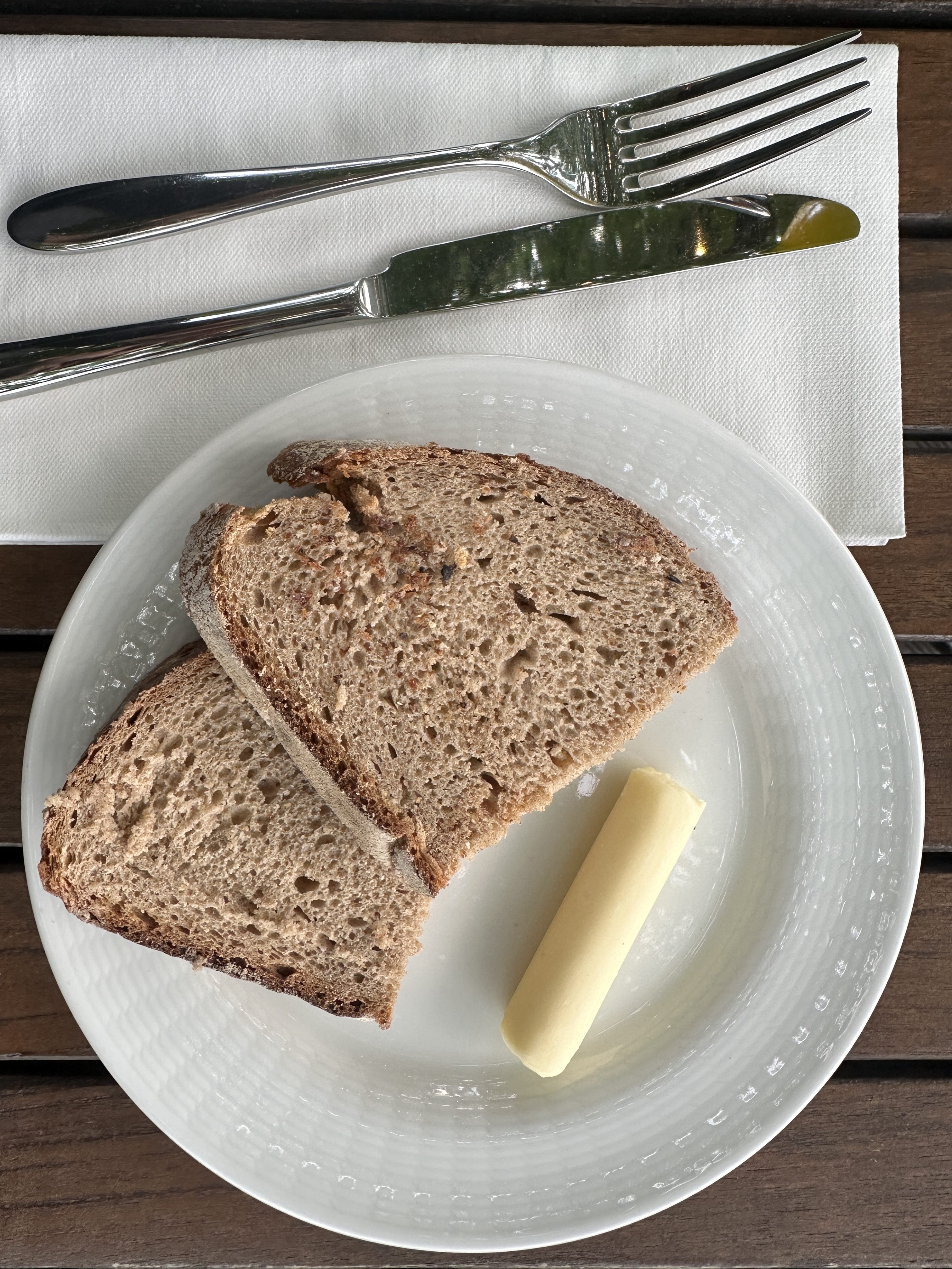 Two pieces of bread and a slice of butter in a white plate on the table.