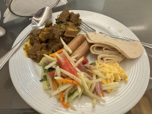A plate of food with curry, sausages, flatbread, salad, and scrambled eggs.