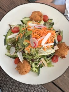 A colourful garden salad featuring fresh greens, cucumber slices, cherry tomatoes, radish, and shredded carrots, topped with crispy breaded cheese balls for a crunchy and creamy contrast.