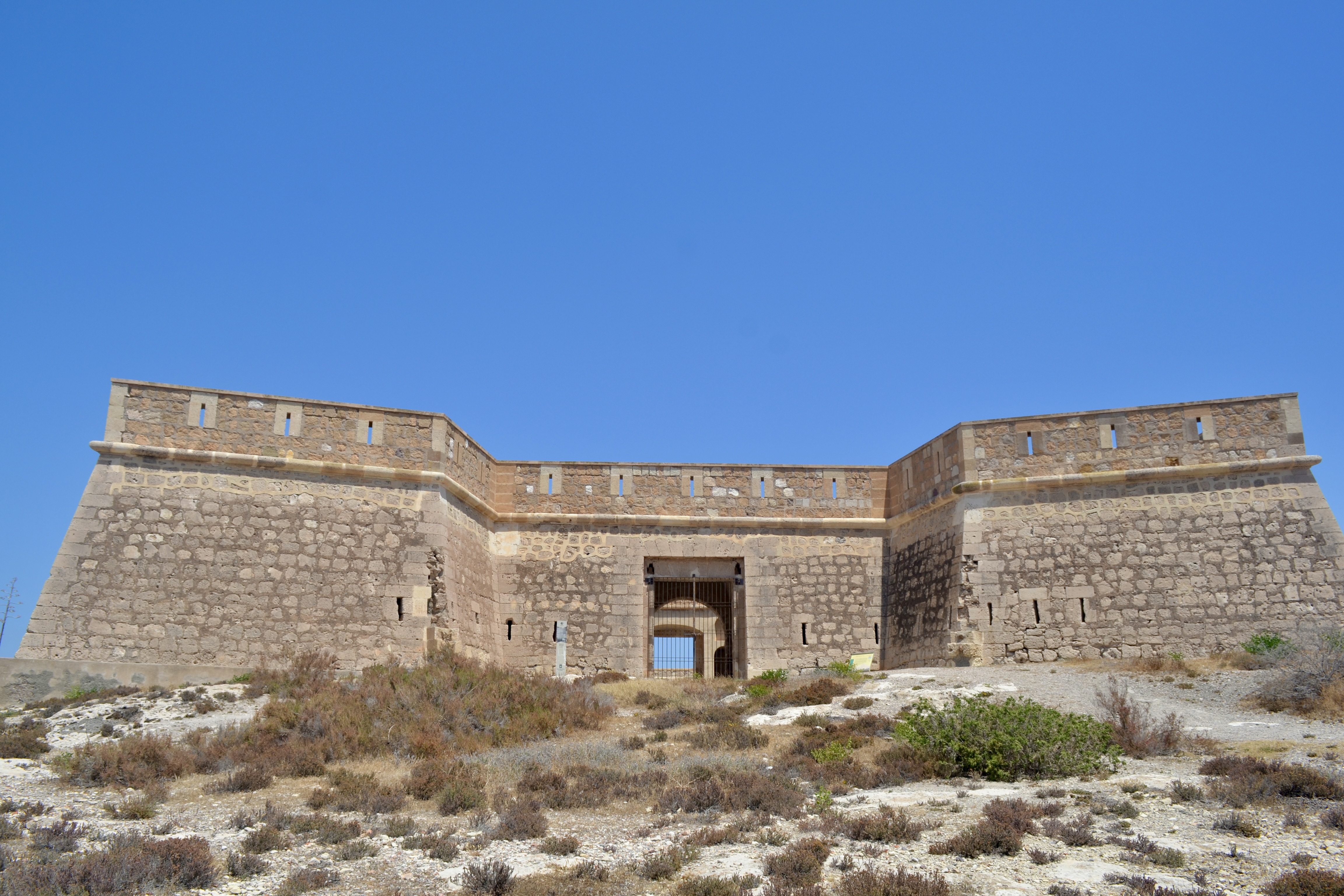 Castillo de San Felipe, a historic stone fortress near Los Escullos, Almería, Spain, stands on a dry hill under a clear blue sky.