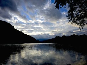 A serene landscape featuring a calm body of water reflecting a dramatic sky filled with clouds.