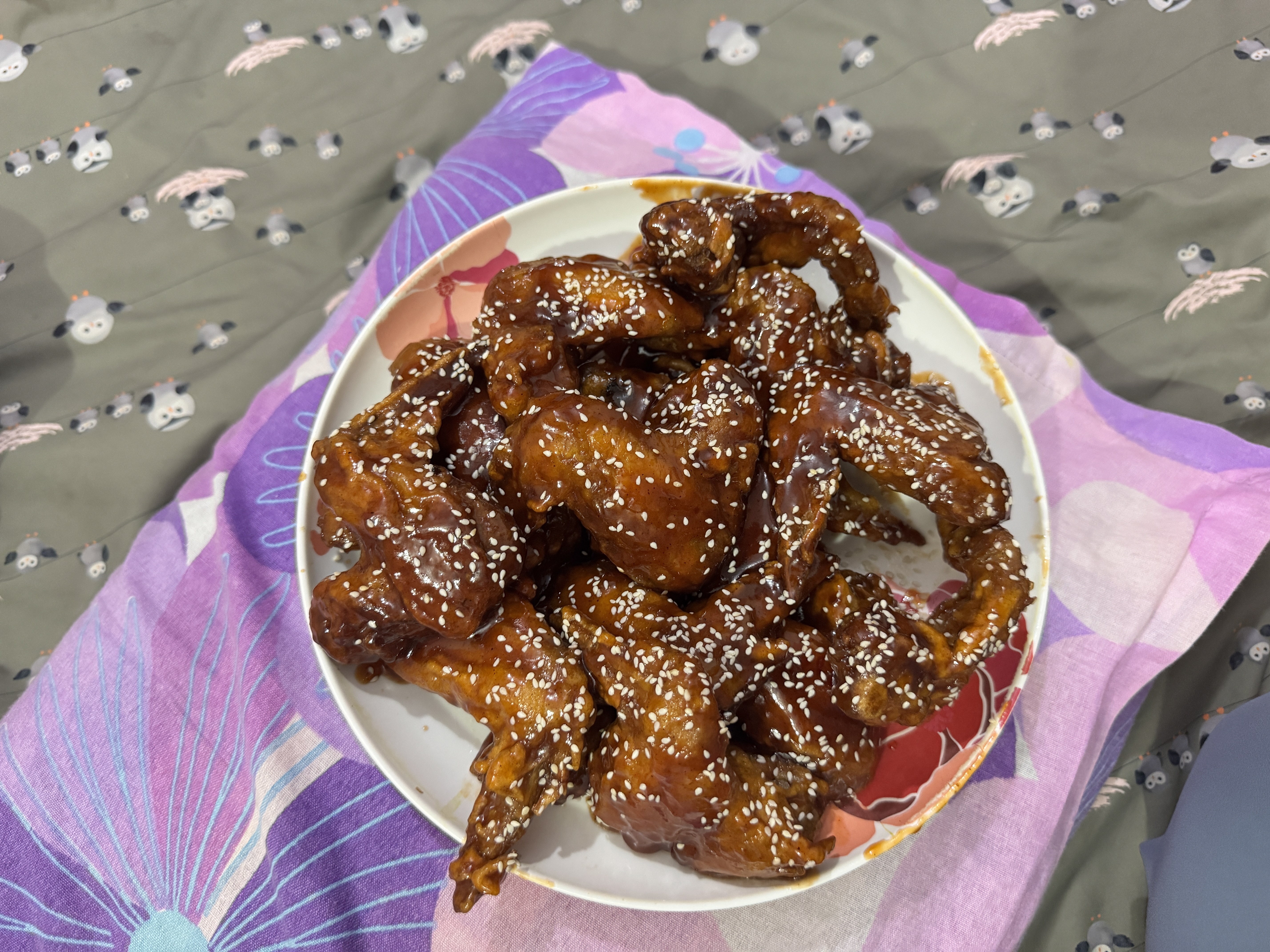 A close-up view of a plate filled with crispy, dark brown fried chicken pieces coated in a shiny, sweet sauce and sprinkled with sesame seeds