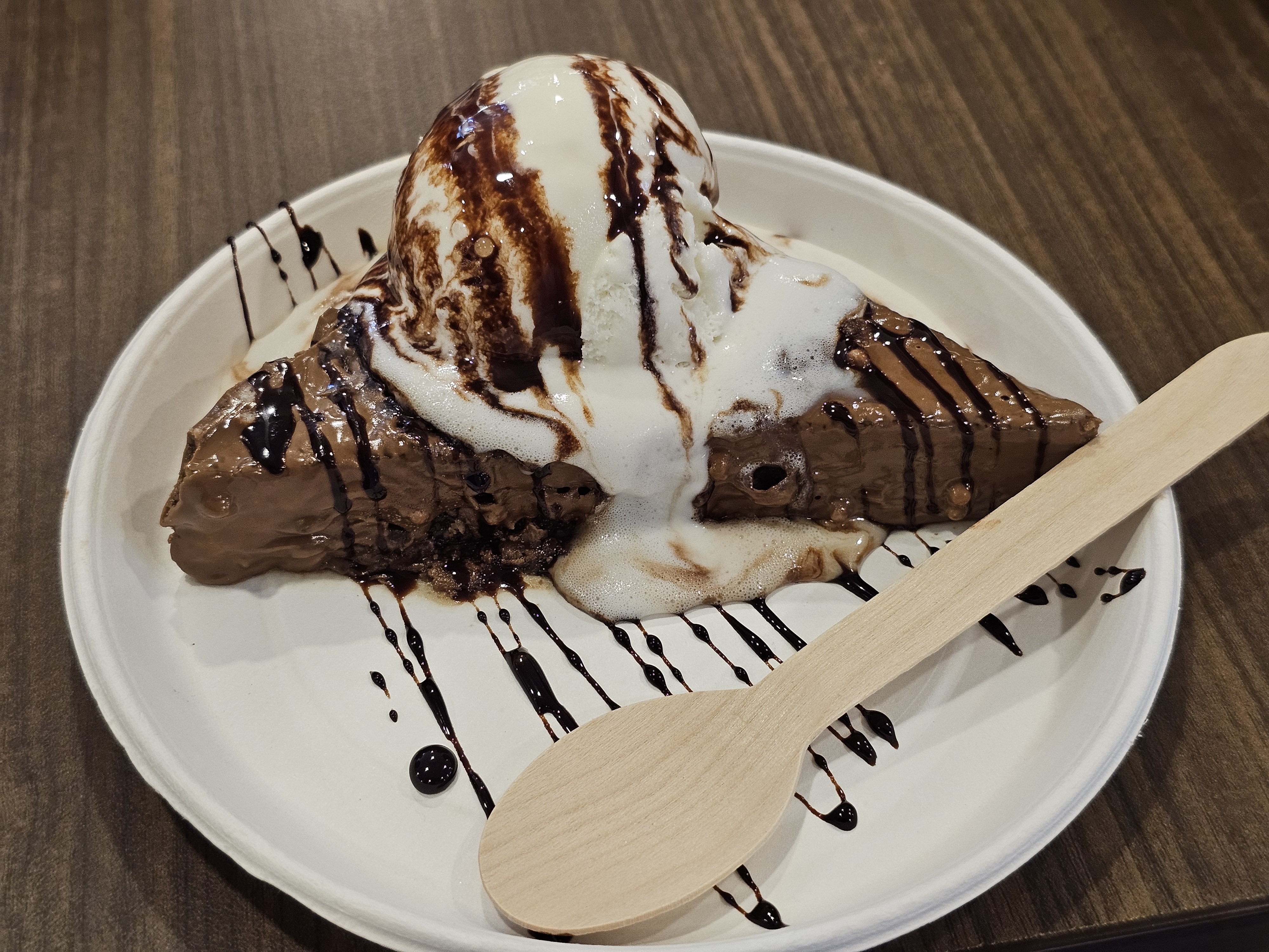 Chocolate Milky Bar topped with vanilla ice cream and chocolate syrup, served on a white plate with a wooden spoon. Captured in Kozhikode, Kerala.