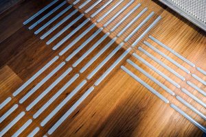 A close-up view of a wooden floor featuring a pattern of thin, plastic strips arranged in a grid for accessibility aid purposes