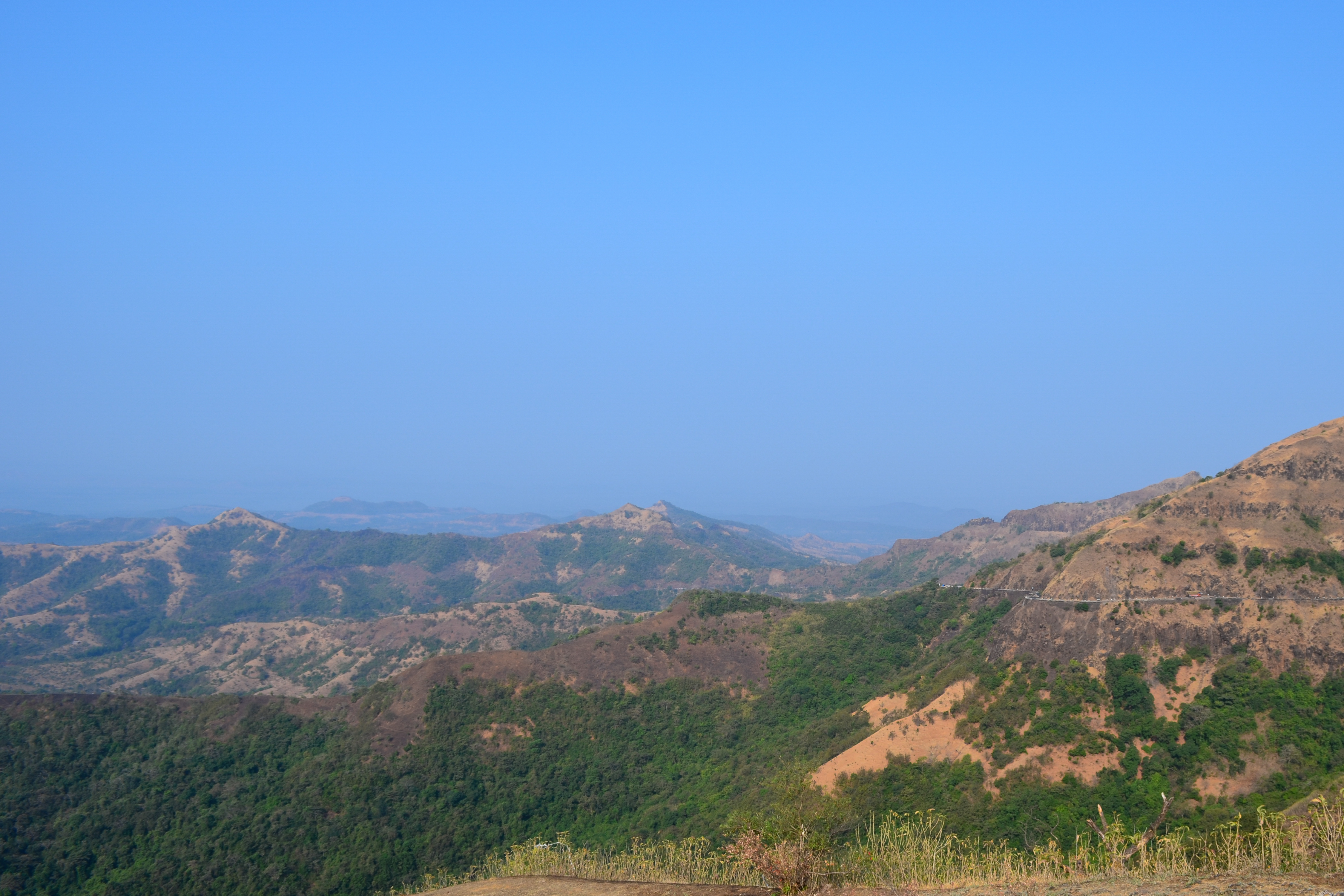 A panoramic view of a majestic mountain range under a clear blue sky, showcasing rugged peaks and lush valleys.