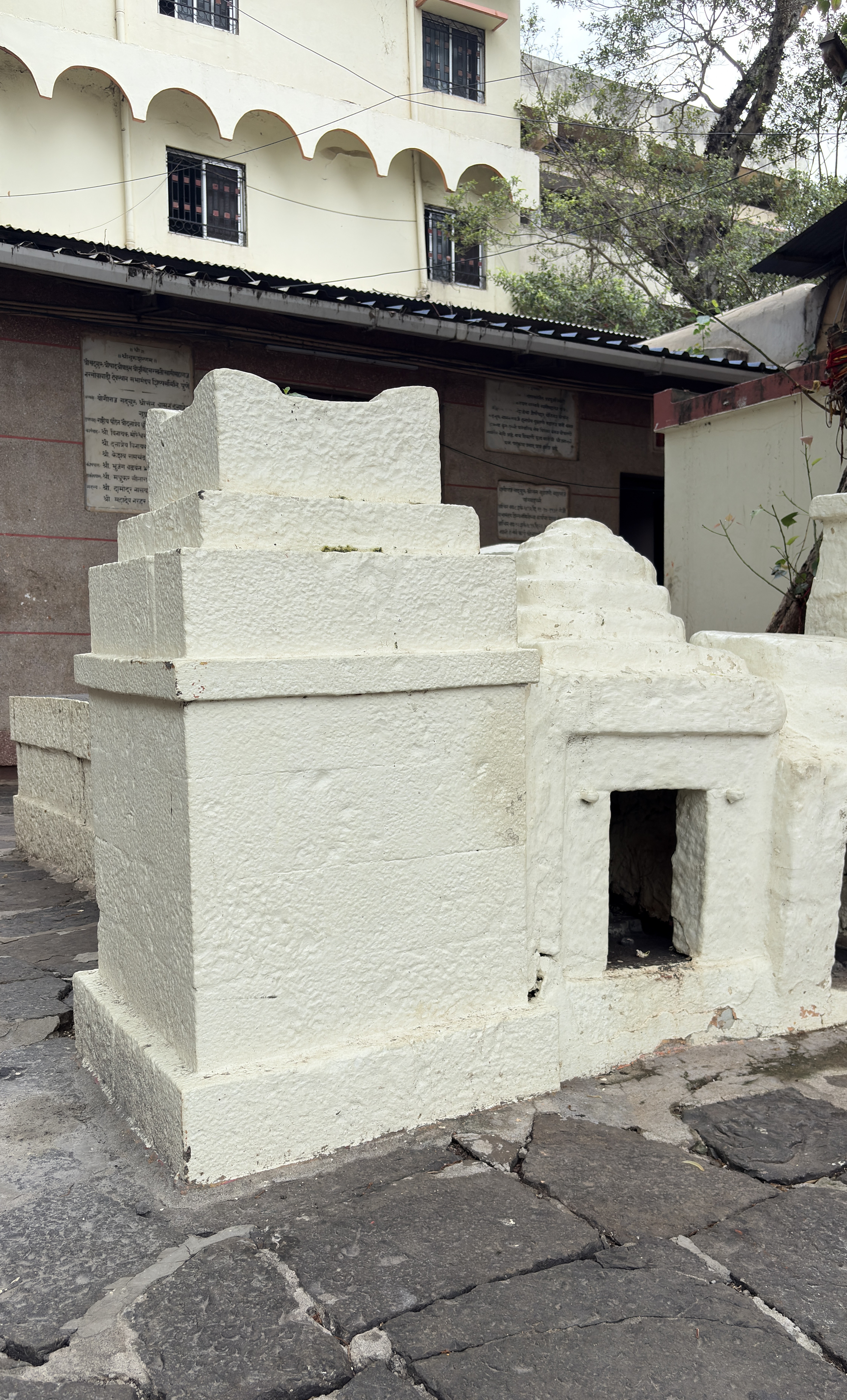 A white, solid stone structure resembling a small shrine is shown in the foreground, with several stepped layers at the top and a small entrance at the base