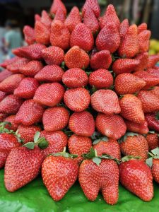 A vibrant pile of fresh red strawberries with green leaves on display at a market in Pune, Maharashtra.