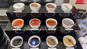 A buffet counter with bowls of sauces, nuts, and toppings.

