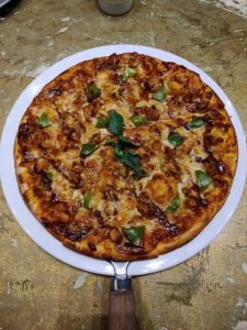 A freshly baked pizza sits on a white plate, featuring a golden crust topped with melted cheese, chunks of green pepper, and pieces of meat. 