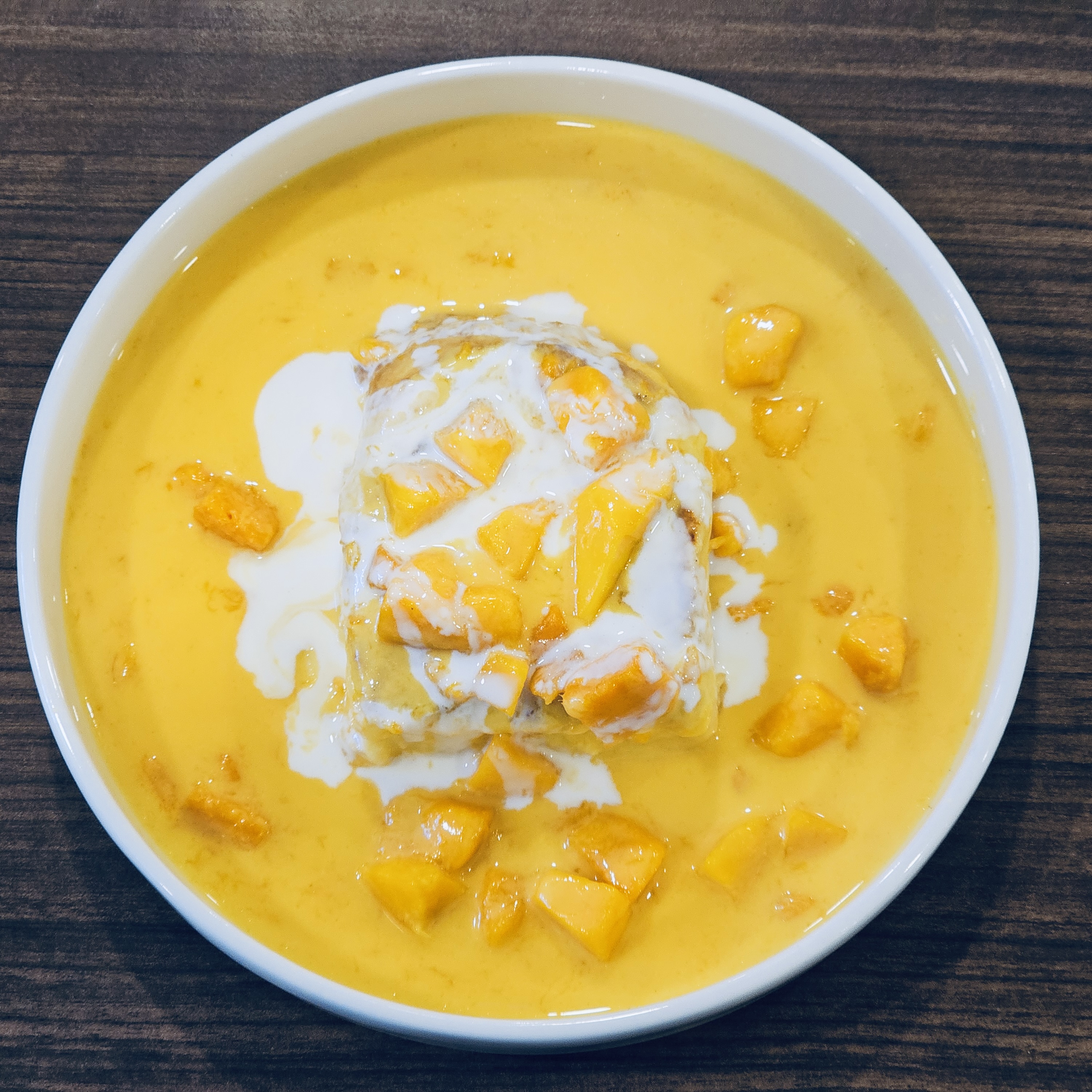 A vibrant yellow mango dessert with fresh mango, thick sauce, and almond milk, served in a white bowl. Captured in Kozhikode, Kerala.